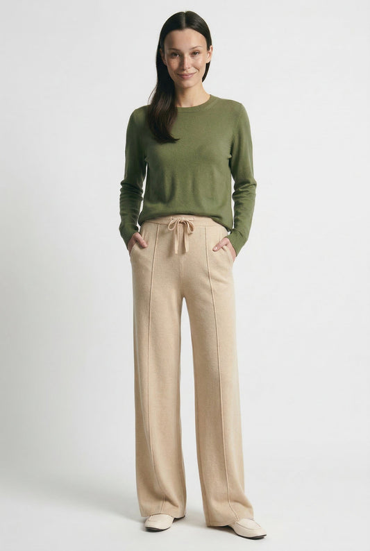 Kvinde iført olivengrøn sweater og beige vide bukser med snørelukning i taljen, stående i naturligt lys._6