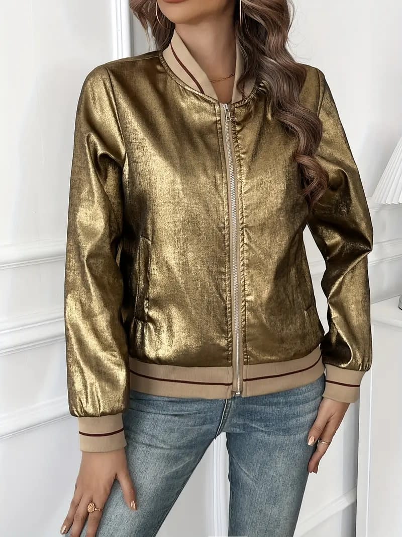 Kvinde iført en guldfarvet metallic bomberjakke med lynlås og ribkant, kombineret med hvid top og jeans._4