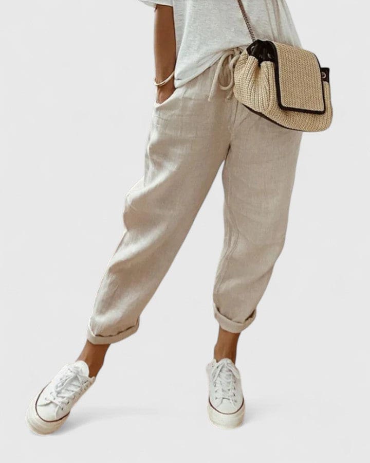 Kvinde iført løse, lyse bukser med elastisk talje, oprullede benafslutninger og hvide sneakers, set fra siden._0