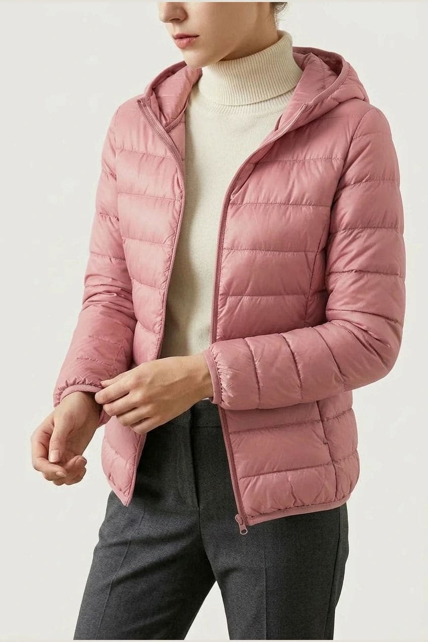 Kvinde i en let quiltet hættejakke med lynlås, båret åben over en rullekravesweater og mørke bukser._12