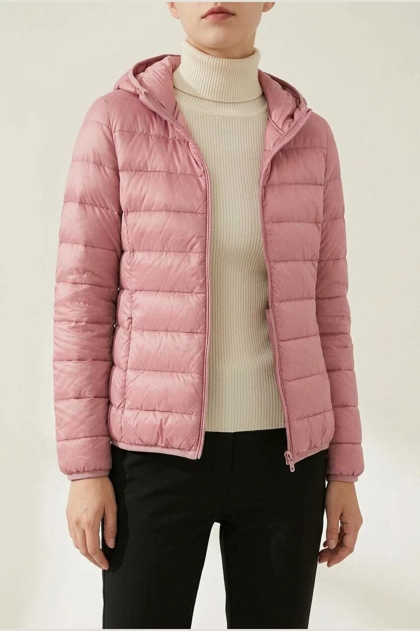 Kvinde i en let quiltet hættejakke med lynlås, båret åben over en rullekravesweater og mørke bukser._13
