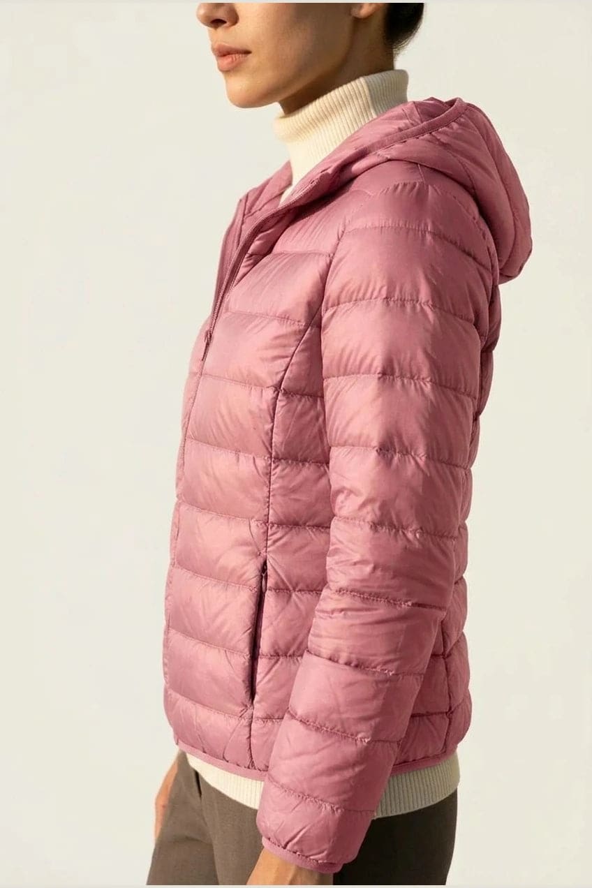 Kvinde i en let quiltet hættejakke med lynlås, båret åben over en rullekravesweater og mørke bukser._14