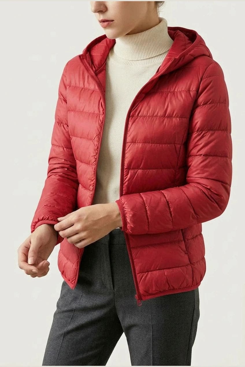 Kvinde i en let quiltet hættejakke med lynlås, båret åben over en rullekravesweater og mørke bukser._17