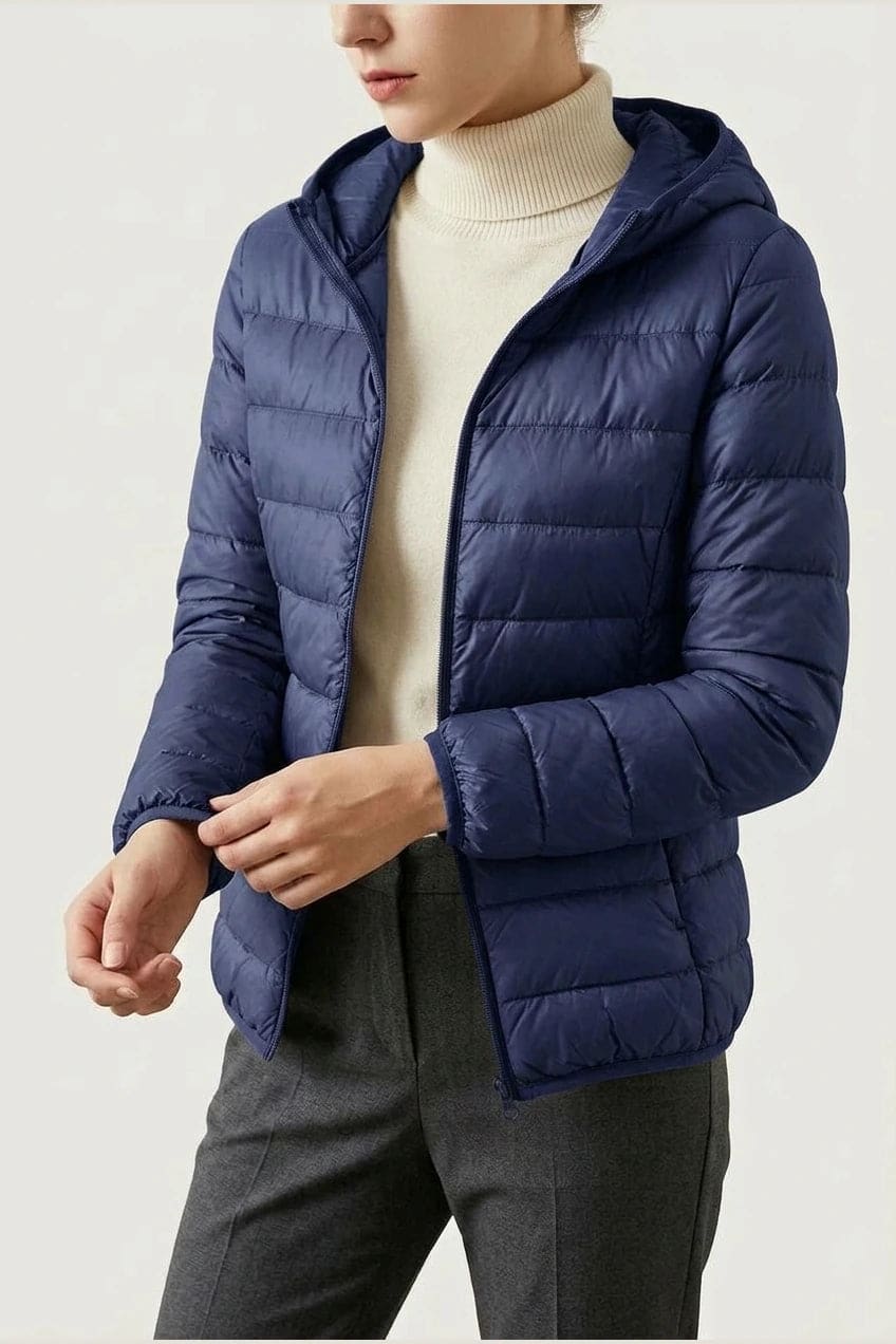 Kvinde i en let quiltet hættejakke med lynlås, båret åben over en rullekravesweater og mørke bukser._2
