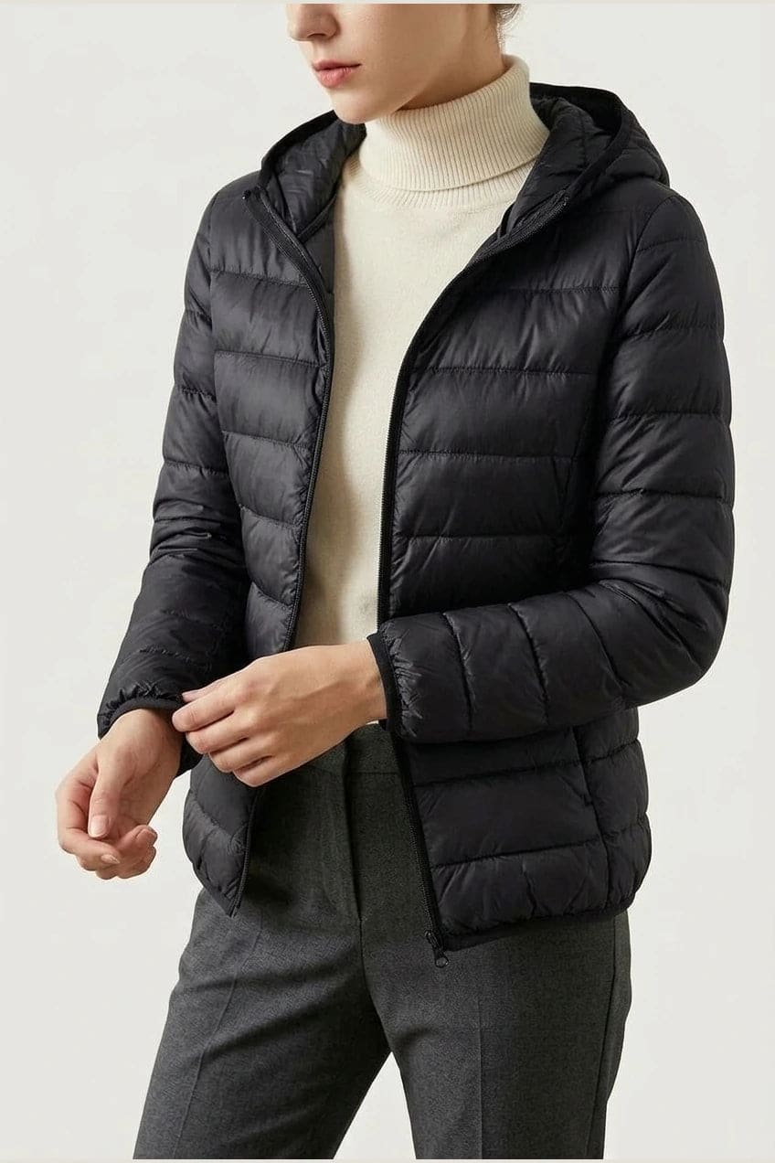 Kvinde i en let quiltet hættejakke med lynlås, båret åben over en rullekravesweater og mørke bukser._7