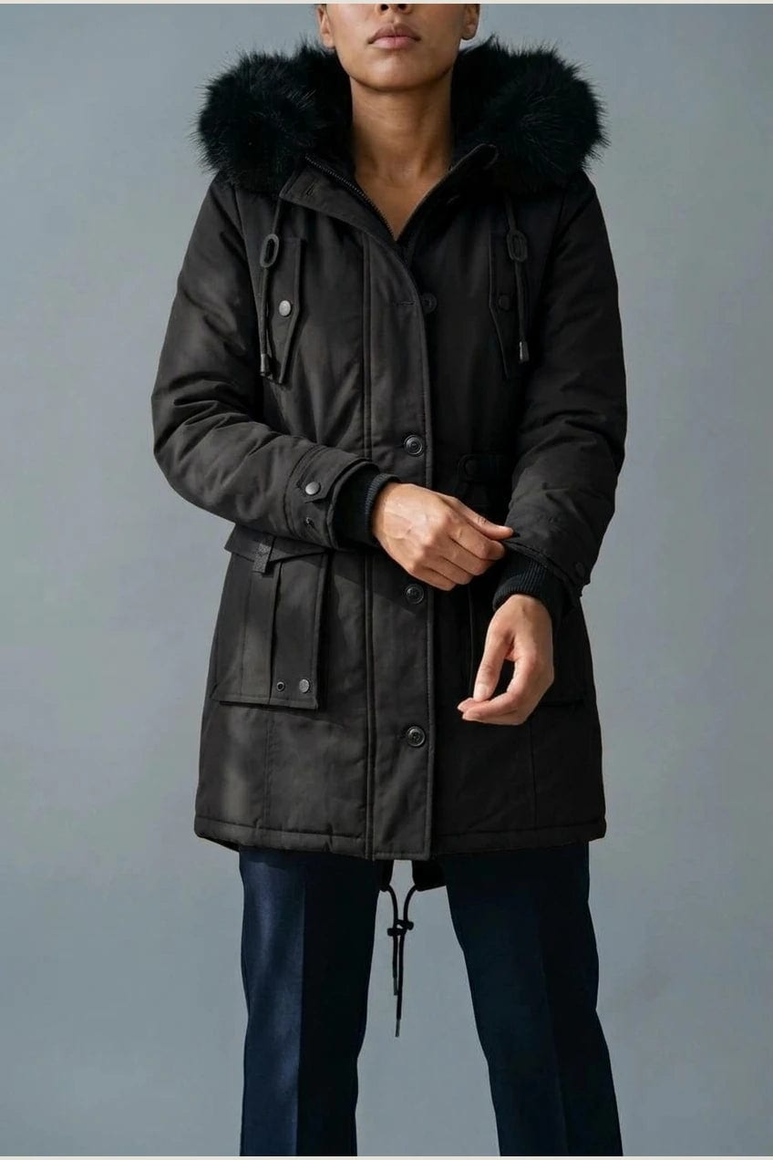 Kvinde i lang vatteret parka med pelskant på hætten, knaprække, taljebånd og fire klaplommer, styles med jeans og støvler._1