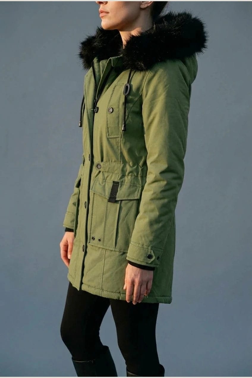 Kvinde i lang vatteret parka med pelskant på hætten, knaprække, taljebånd og fire klaplommer, styles med jeans og støvler._10