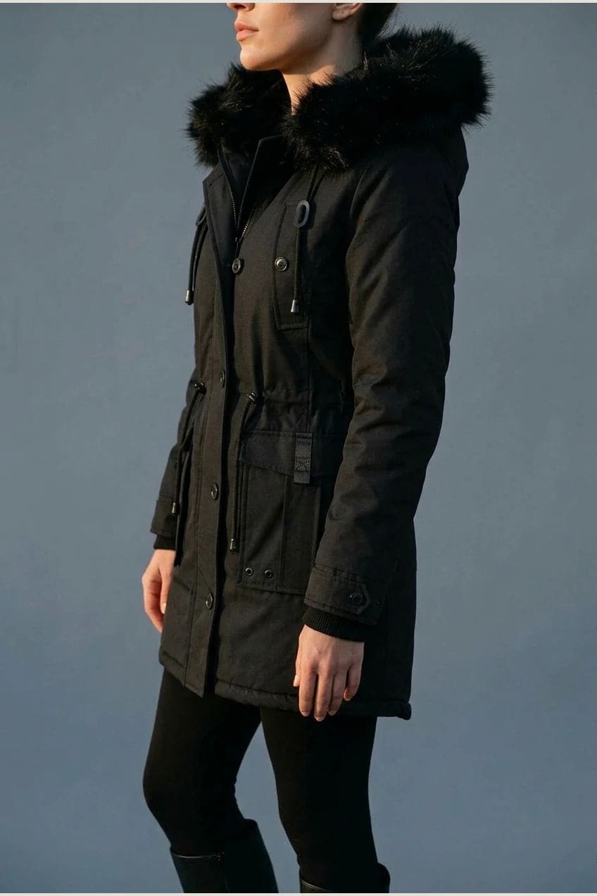 Kvinde i lang vatteret parka med pelskant på hætten, knaprække, taljebånd og fire klaplommer, styles med jeans og støvler._4