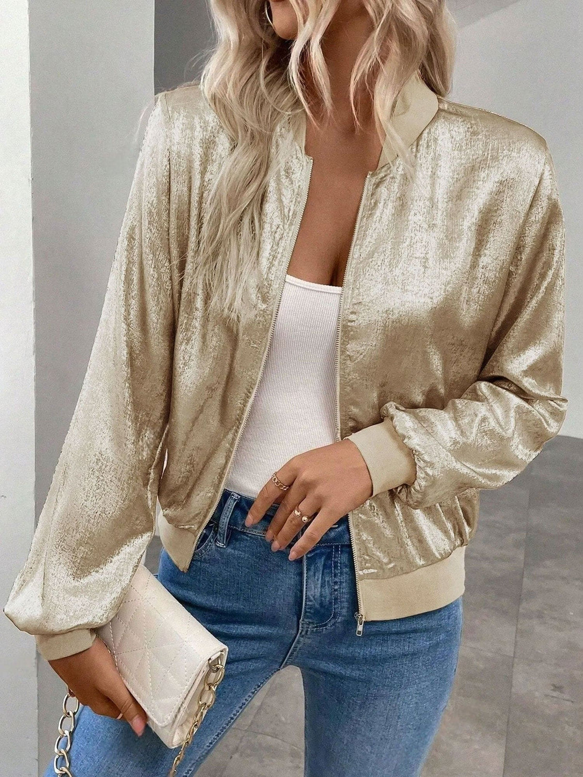 Kvinde iført kort bomber jakke med shimmer-finish og lynlås foran, stylet med hvid top og jeans_2