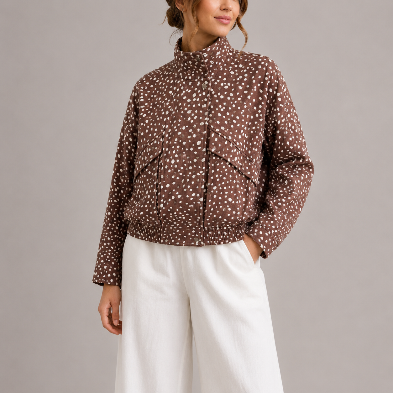 Kvinde iført en kort bomber jakke med polkaprikker print og høj krave, stylet med hvide bukser mod neutral baggrund._0