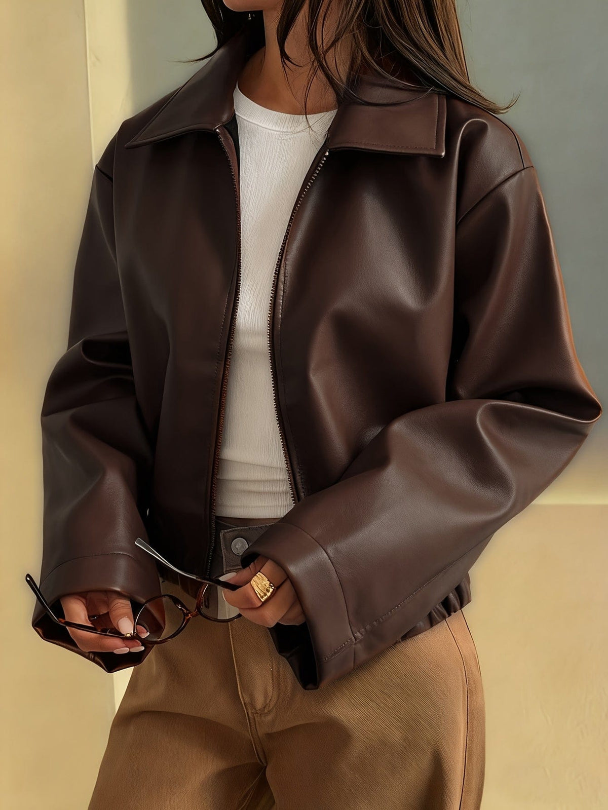 Kvinde iført brun cropped jakke med krave og lynlås, stylet med hvid striktrøje og beige bukser_0