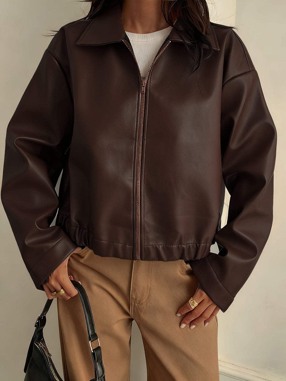 Kvinde iført brun cropped jakke med krave og lynlås, stylet med hvid striktrøje og beige bukser_1