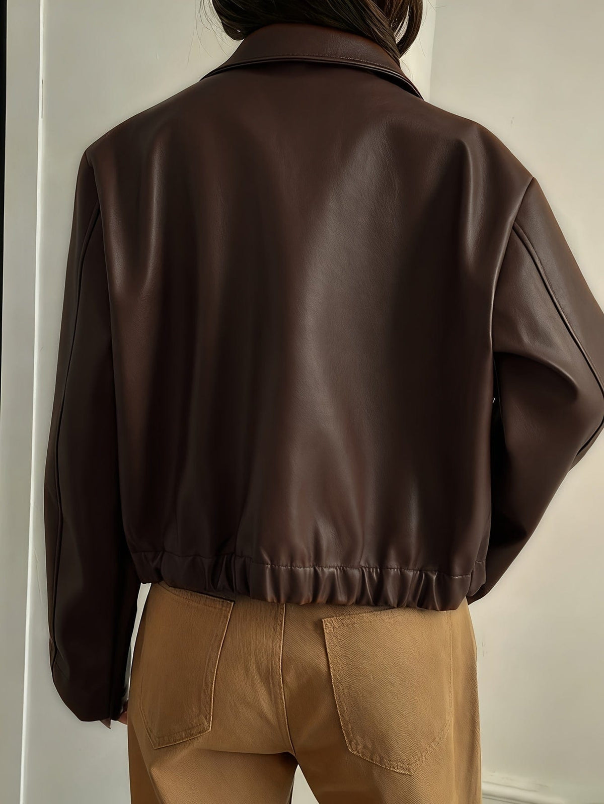 Kvinde iført brun cropped jakke med krave og lynlås, stylet med hvid striktrøje og beige bukser_2