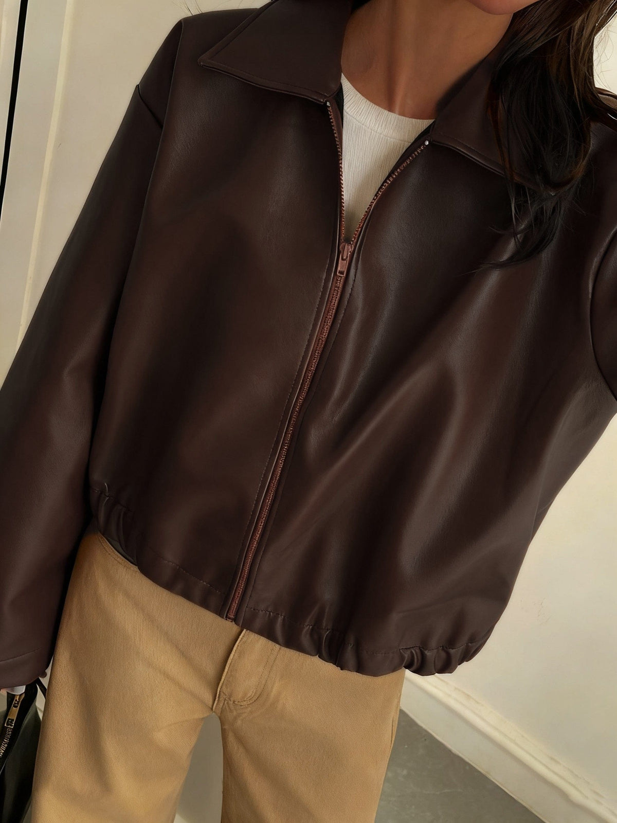 Kvinde iført brun cropped jakke med krave og lynlås, stylet med hvid striktrøje og beige bukser_4