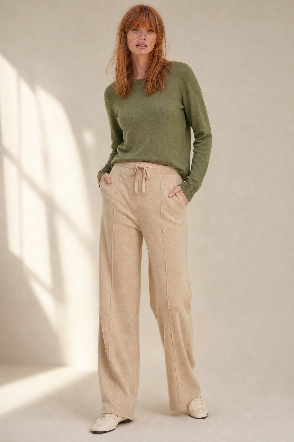 Kvinde iført olivengrøn sweater og beige vide bukser med snørelukning i taljen, stående i naturligt lys._0