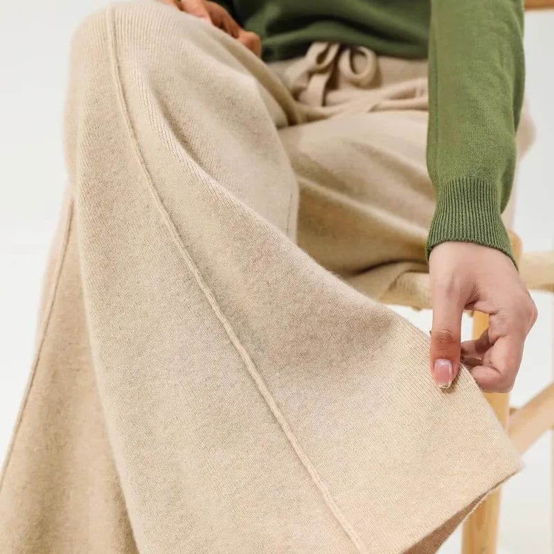 Kvinde iført olivengrøn sweater og beige vide bukser med snørelukning i taljen, stående i naturligt lys._10