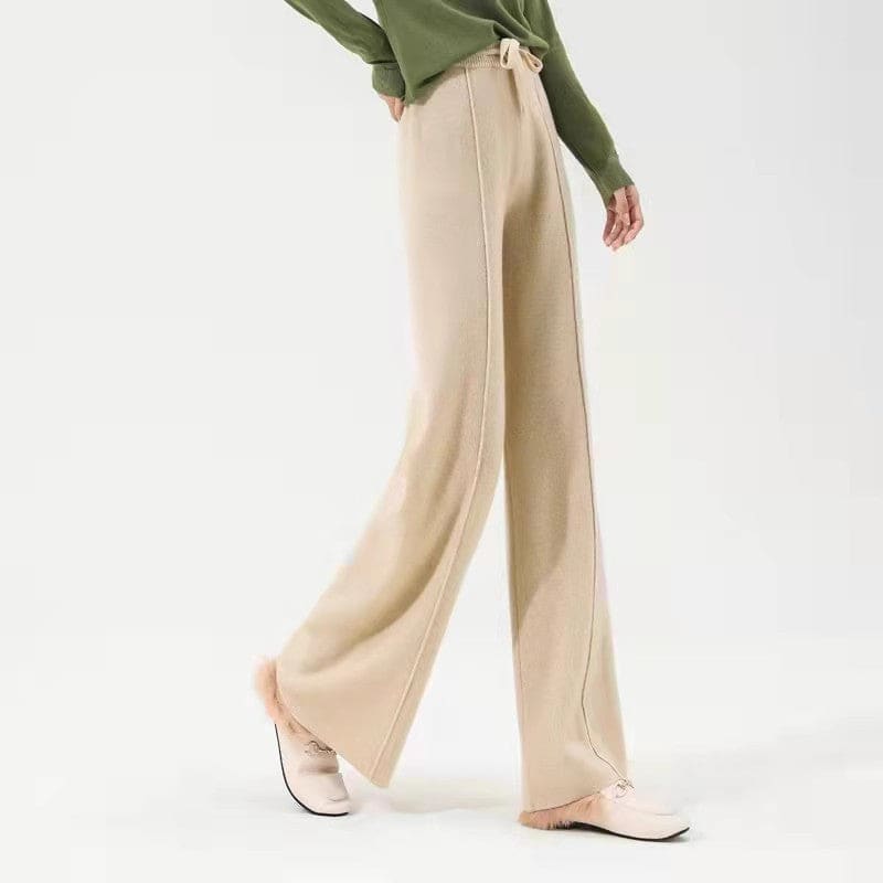 Kvinde iført olivengrøn sweater og beige vide bukser med snørelukning i taljen, stående i naturligt lys._11