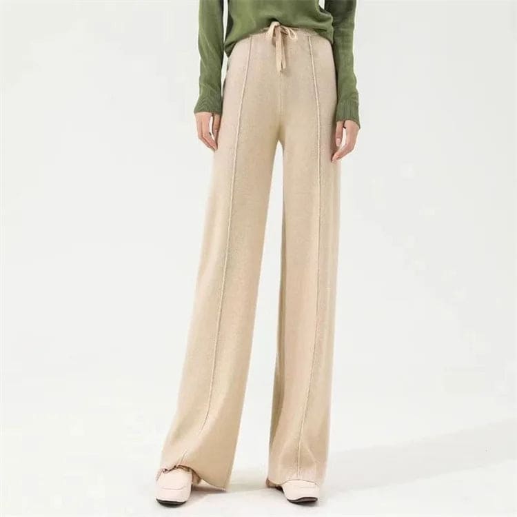 Kvinde iført olivengrøn sweater og beige vide bukser med snørelukning i taljen, stående i naturligt lys._12