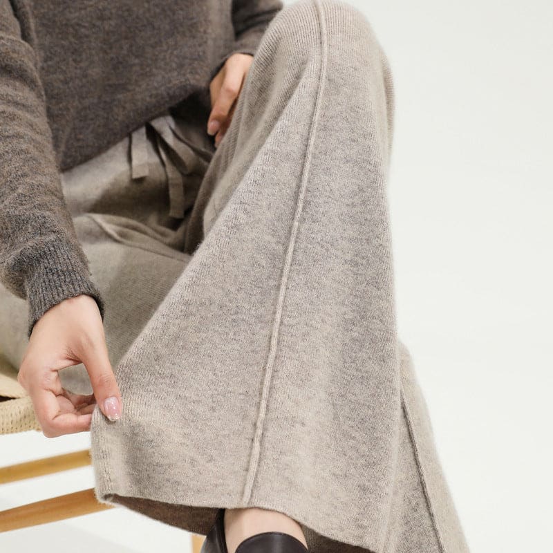 Kvinde iført olivengrøn sweater og beige vide bukser med snørelukning i taljen, stående i naturligt lys._13