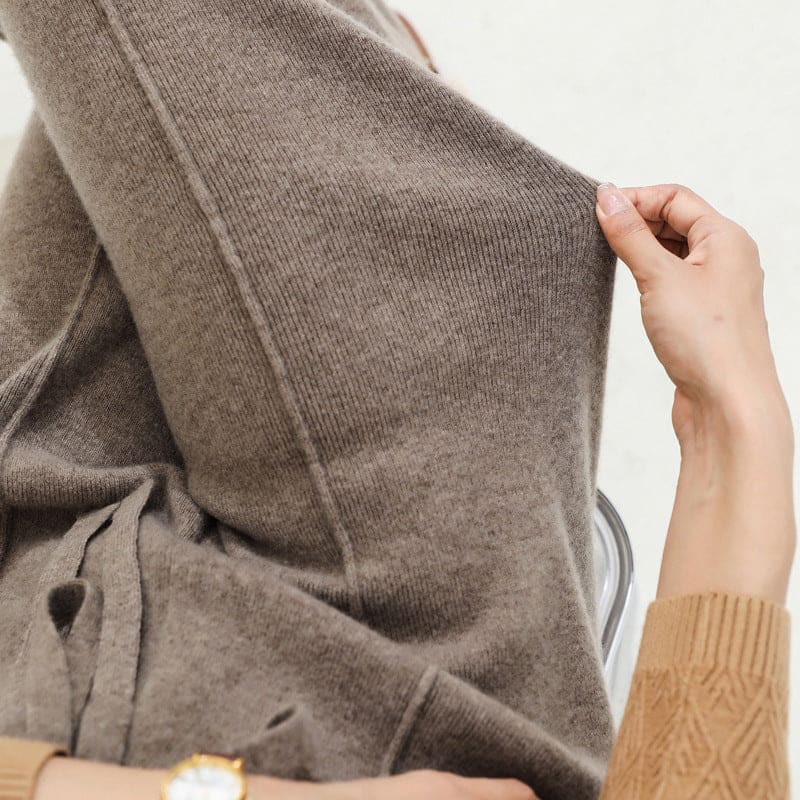 Kvinde iført olivengrøn sweater og beige vide bukser med snørelukning i taljen, stående i naturligt lys._14