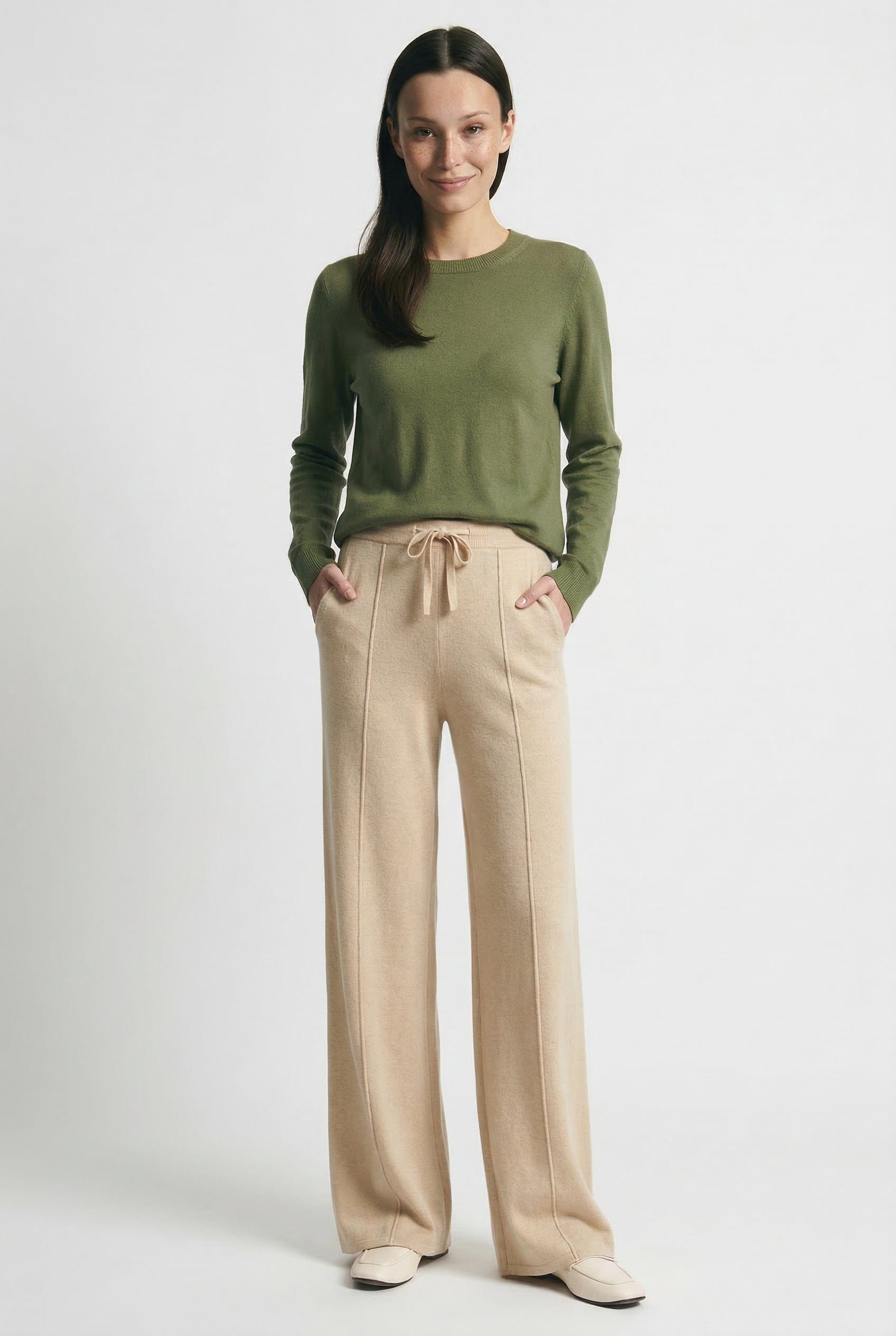 Kvinde iført olivengrøn sweater og beige vide bukser med snørelukning i taljen, stående i naturligt lys._6
