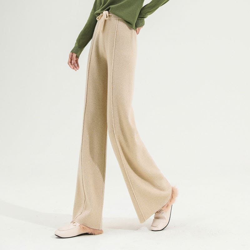 Kvinde iført olivengrøn sweater og beige vide bukser med snørelukning i taljen, stående i naturligt lys._9