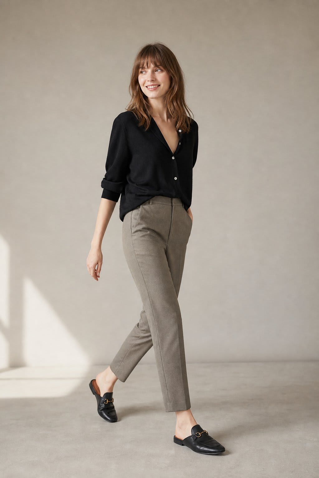 Kvinde iført sorte loafers, grå bukser med høj talje og sort cardigan i neutral kulisse._0