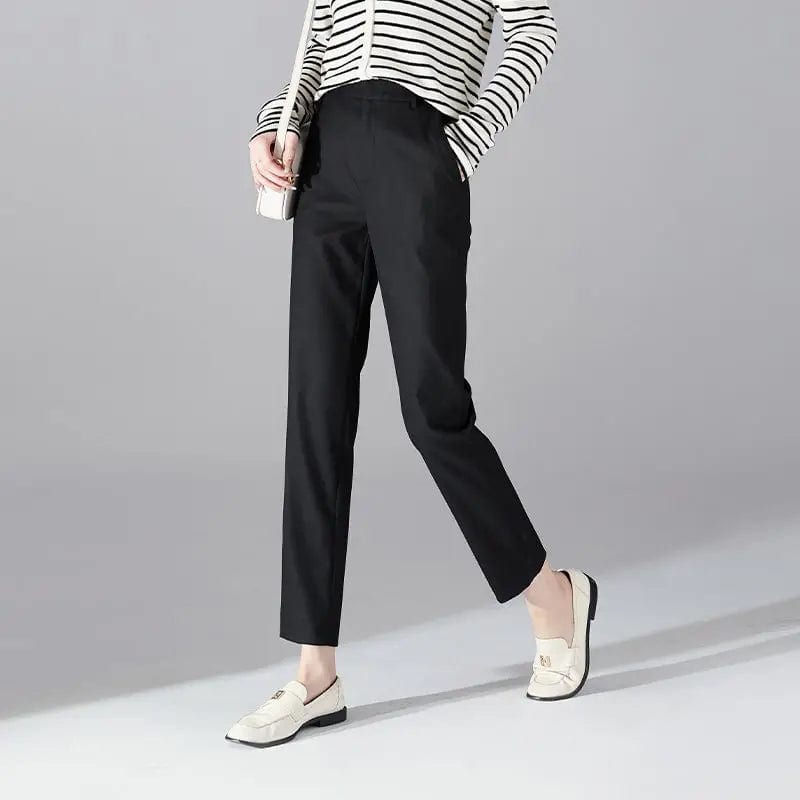 Kvinde iført sorte loafers, grå bukser med høj talje og sort cardigan i neutral kulisse._13