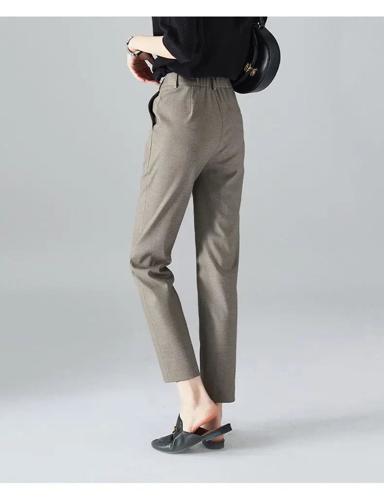 Kvinde iført sorte loafers, grå bukser med høj talje og sort cardigan i neutral kulisse._16