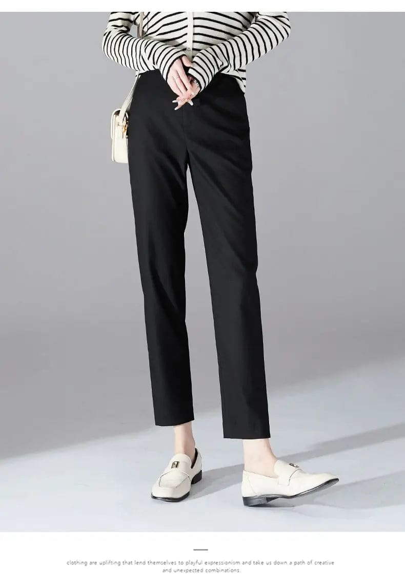 Kvinde iført sorte loafers, grå bukser med høj talje og sort cardigan i neutral kulisse._17