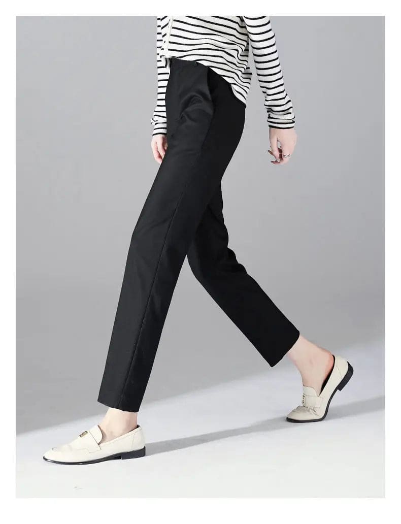 Kvinde iført sorte loafers, grå bukser med høj talje og sort cardigan i neutral kulisse._18