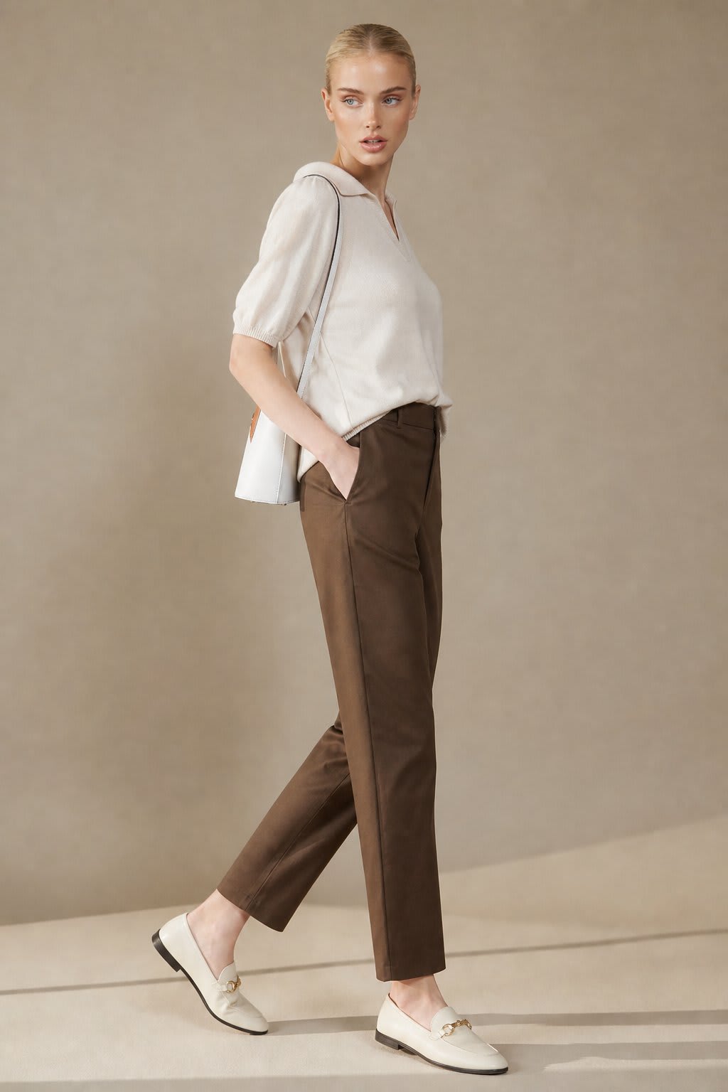 Kvinde iført sorte loafers, grå bukser med høj talje og sort cardigan i neutral kulisse._2