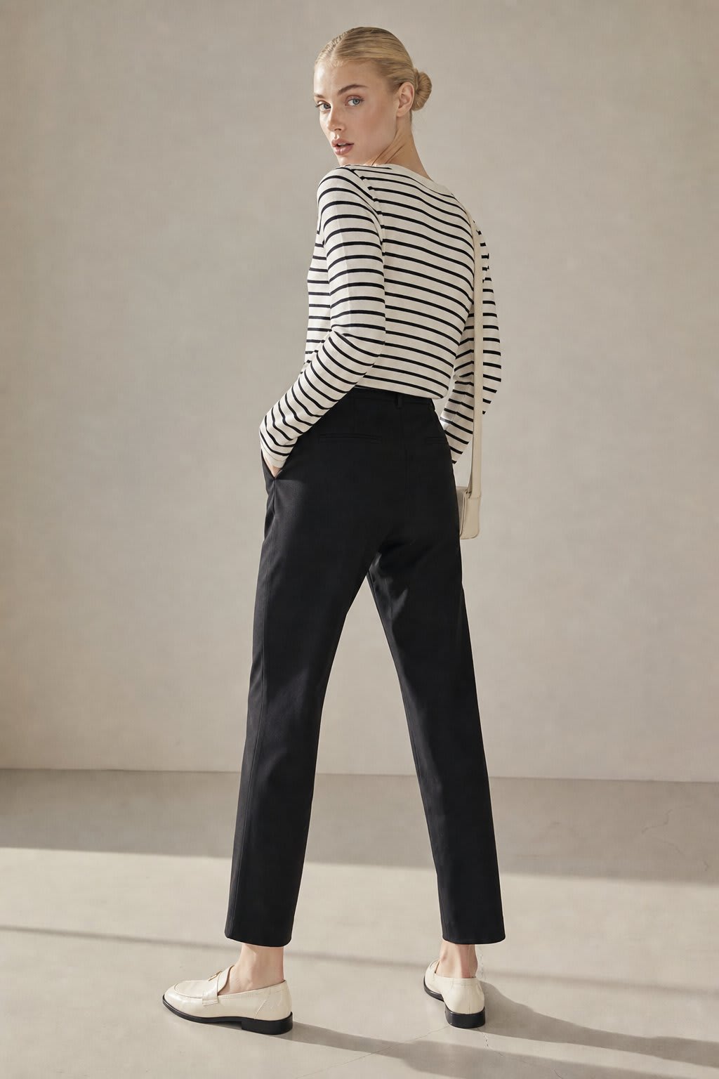 Kvinde iført sorte loafers, grå bukser med høj talje og sort cardigan i neutral kulisse._4