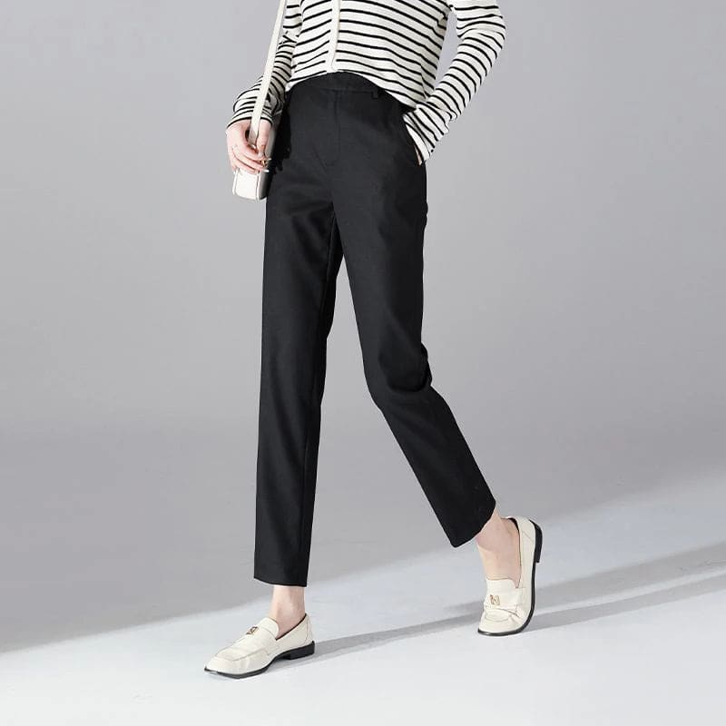 Kvinde iført sorte loafers, grå bukser med høj talje og sort cardigan i neutral kulisse._6