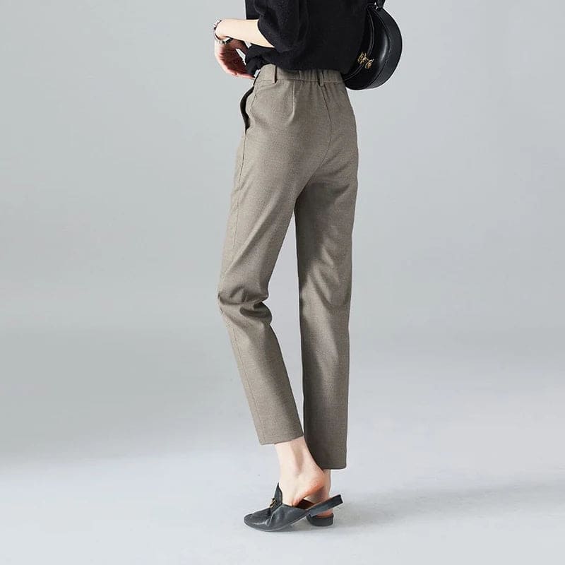 Kvinde iført sorte loafers, grå bukser med høj talje og sort cardigan i neutral kulisse._9