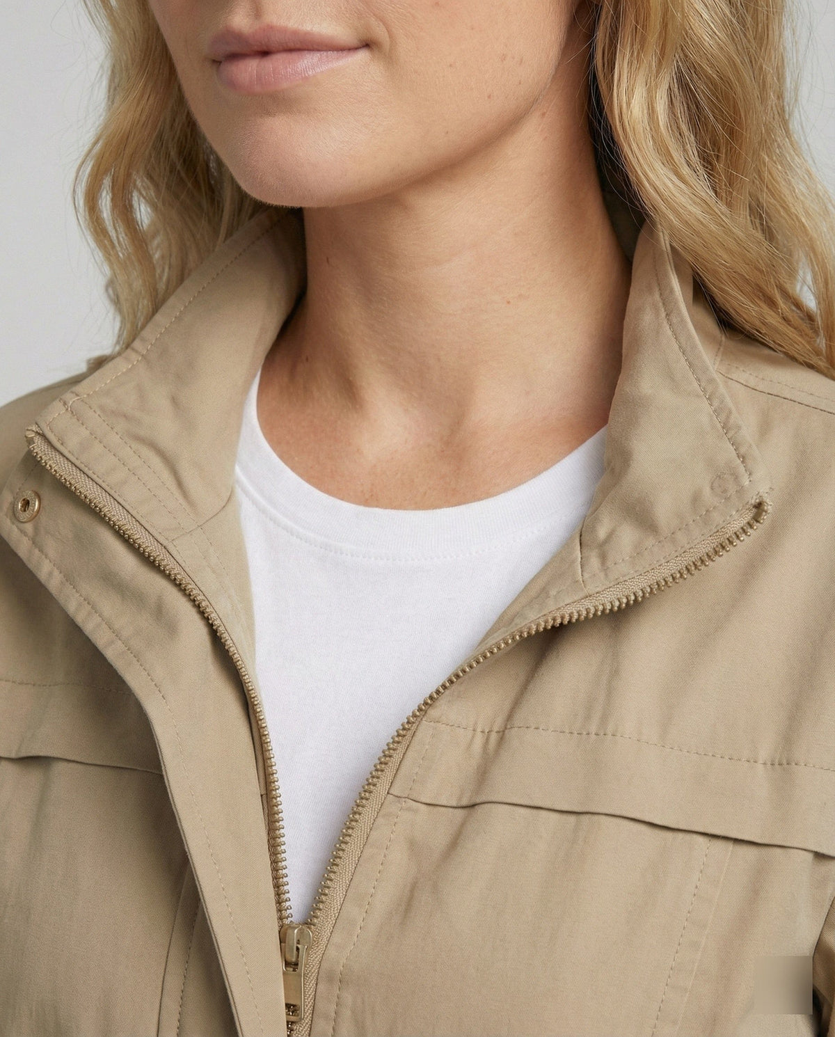 Kvinde i lang utility-jakke med høj krave, lynlås, snøre i taljen og store lommer, styret med jeans og hvid T-shirt._3