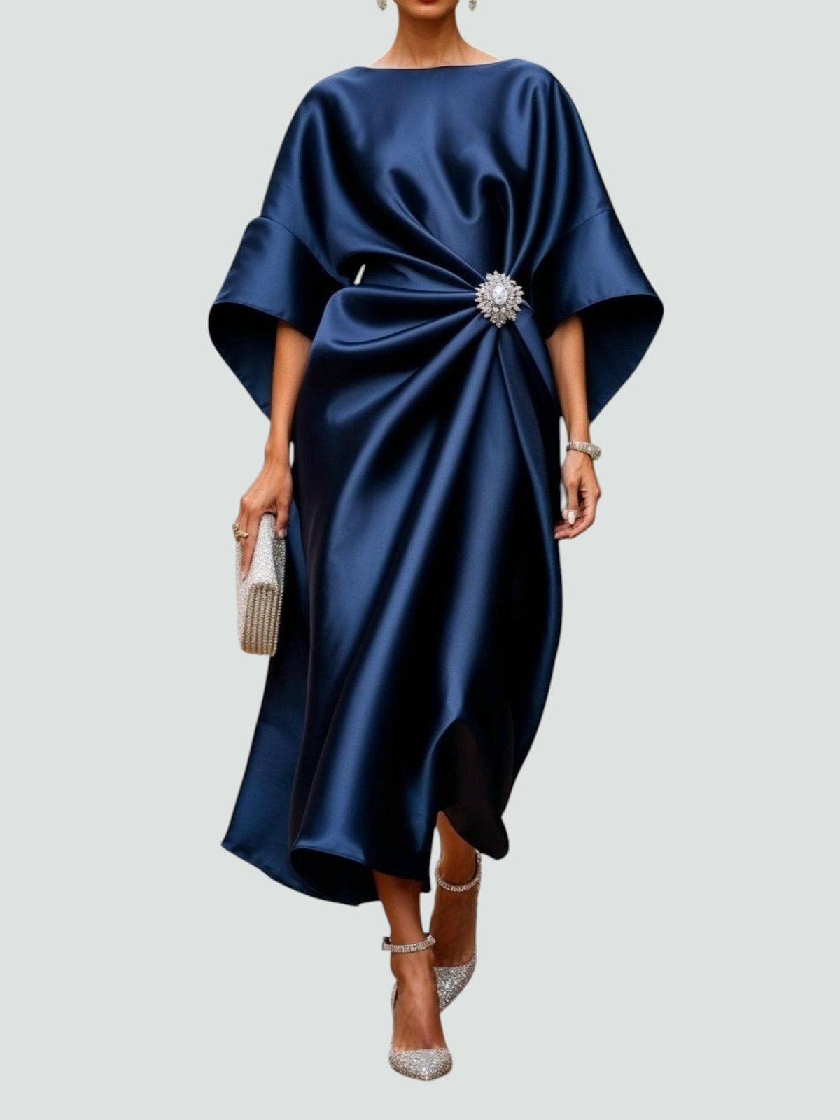 Kvinde iført en elegant midikjole med kimono-inspirerede ærmer, draperet talje og dekorativ broche til festlige anledninger._0