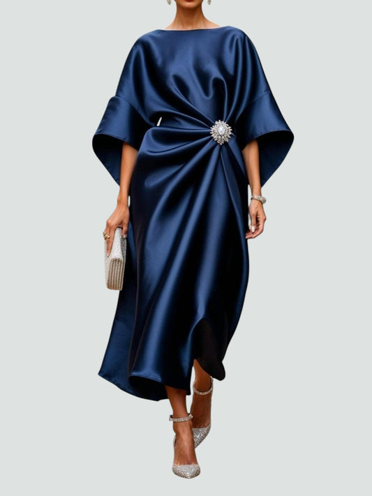 Kvinde iført en elegant midikjole med kimono-inspirerede ærmer, draperet talje og dekorativ broche til festlige anledninger._0