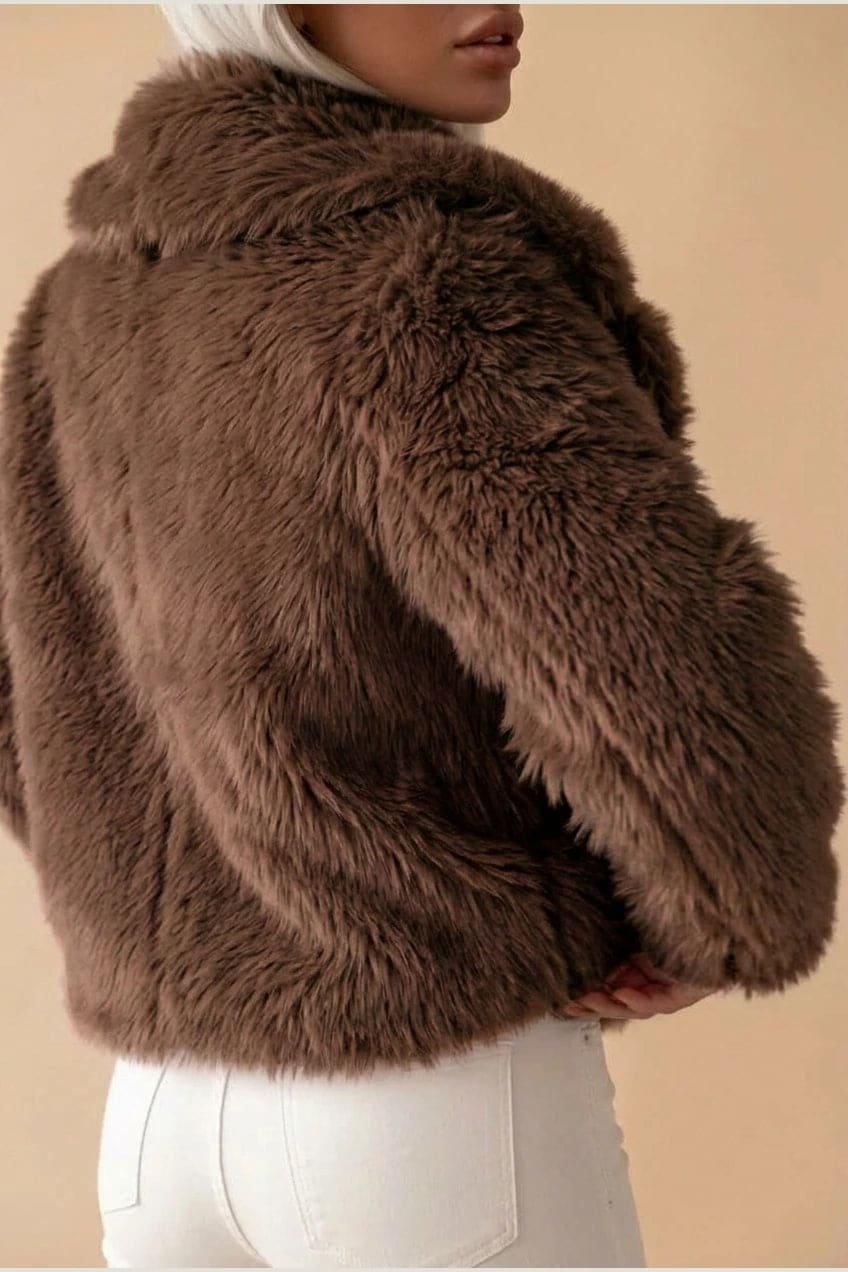 Kort jakke i fake fur med stor krave, åben front og voluminøse ærmer, båret over en enkel top og smalle bukser._2
