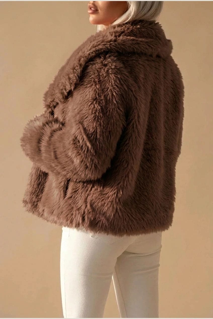 Kort jakke i fake fur med stor krave, åben front og voluminøse ærmer, båret over en enkel top og smalle bukser._3