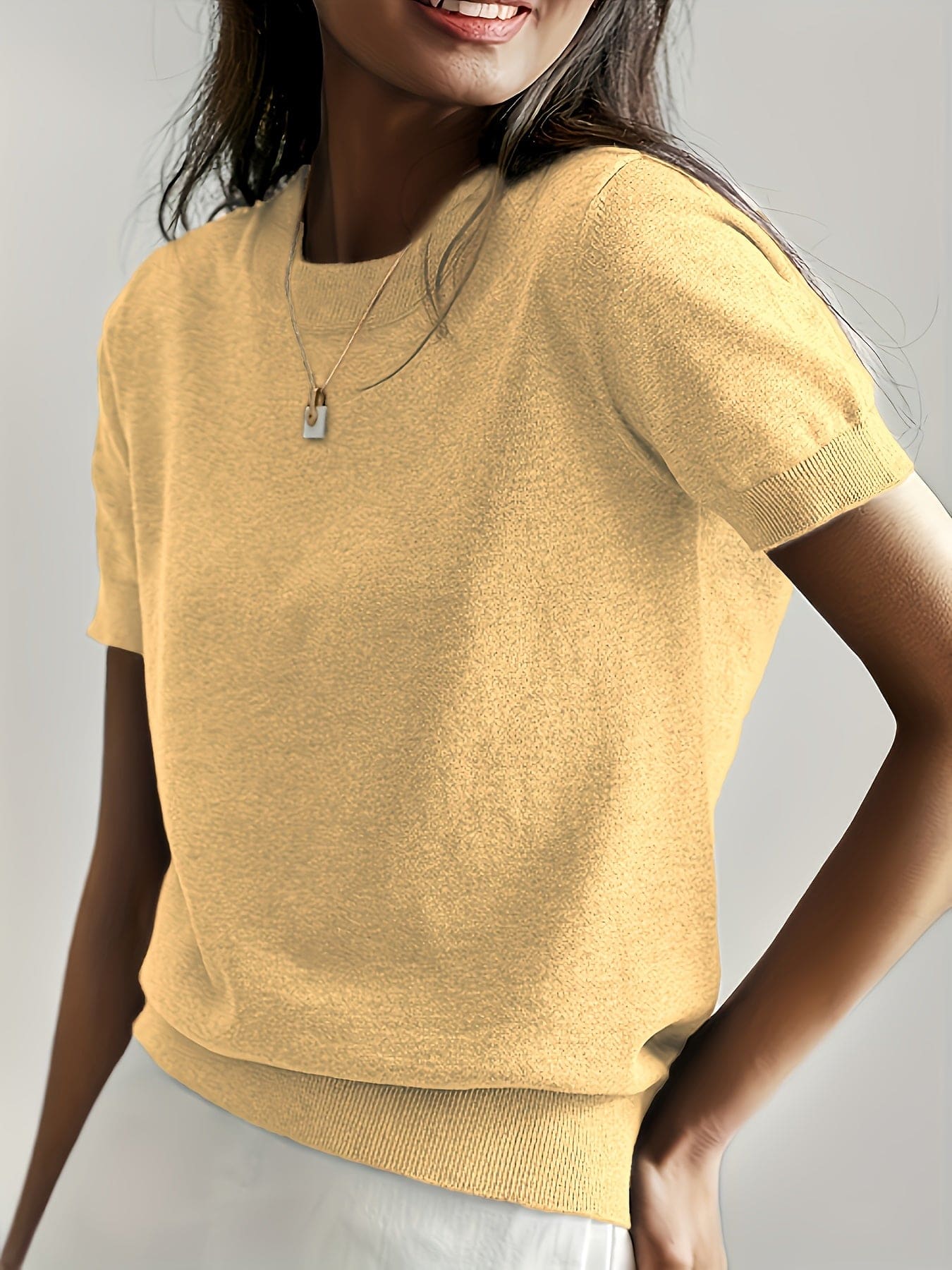 Kvinde iført en fintstrikket kortærmet sweater med rund hals og afslappet pasform, stylet med en lys nederdel og en guldfarvet halskæde._1