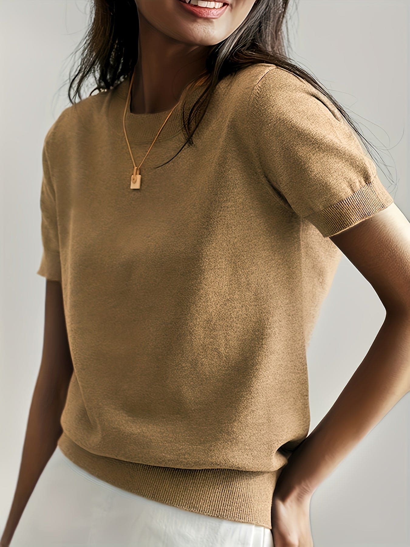 Kvinde iført en fintstrikket kortærmet sweater med rund hals og afslappet pasform, stylet med en lys nederdel og en guldfarvet halskæde._2