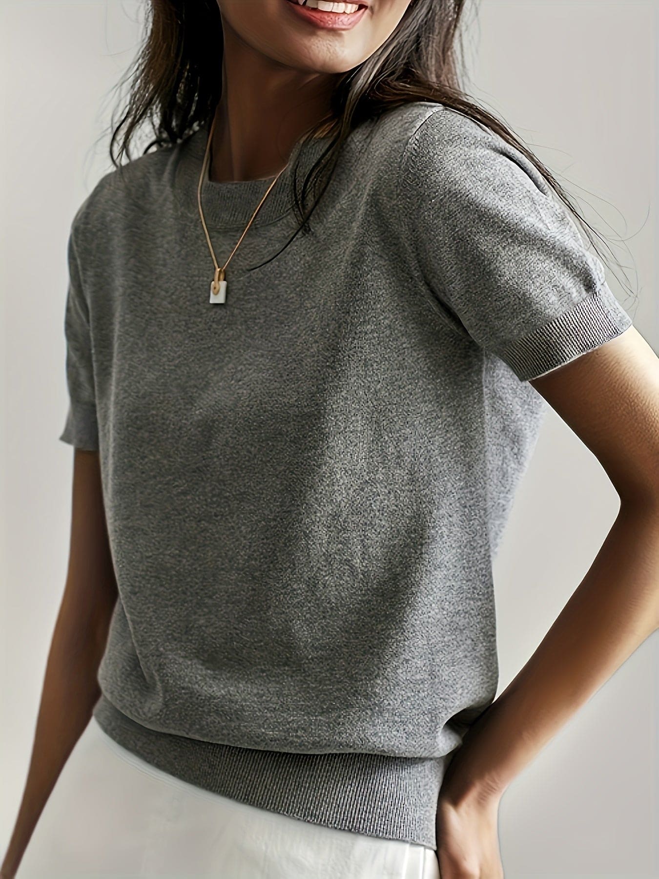 Kvinde iført en fintstrikket kortærmet sweater med rund hals og afslappet pasform, stylet med en lys nederdel og en guldfarvet halskæde._3