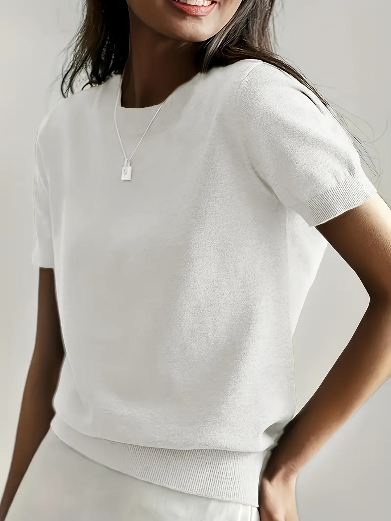 Kvinde iført en fintstrikket kortærmet sweater med rund hals og afslappet pasform, stylet med en lys nederdel og en guldfarvet halskæde._4