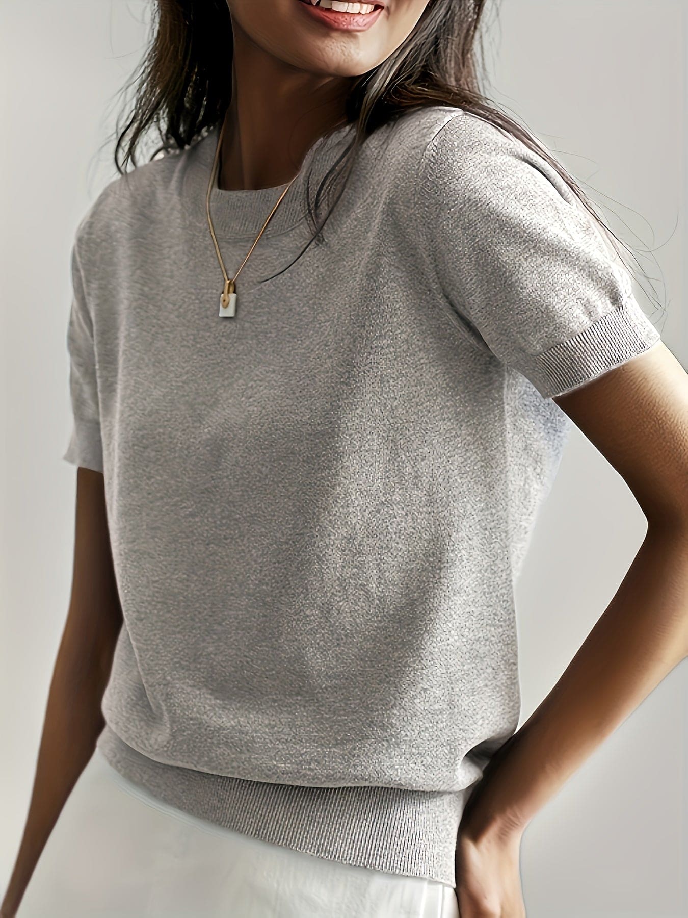 Kvinde iført en fintstrikket kortærmet sweater med rund hals og afslappet pasform, stylet med en lys nederdel og en guldfarvet halskæde._5