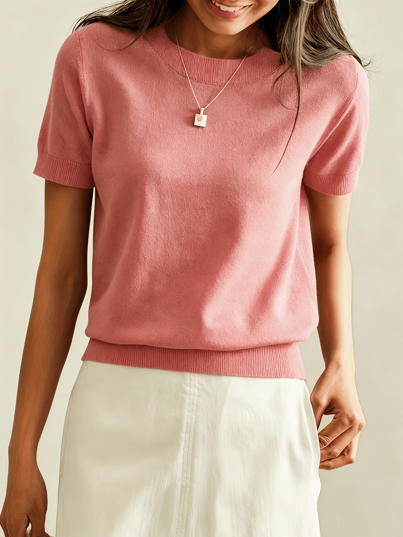 Kvinde iført en fintstrikket kortærmet sweater med rund hals og afslappet pasform, stylet med en lys nederdel og en guldfarvet halskæde._7
