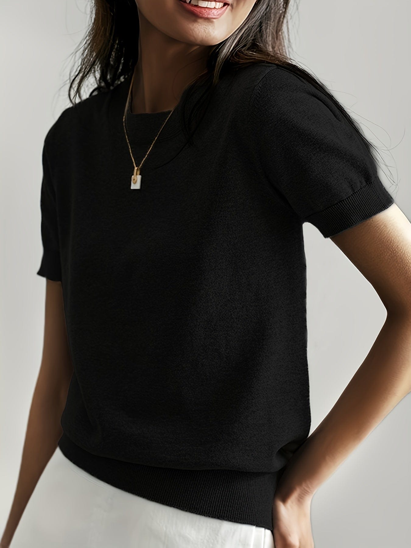 Kvinde iført en fintstrikket kortærmet sweater med rund hals og afslappet pasform, stylet med en lys nederdel og en guldfarvet halskæde._8