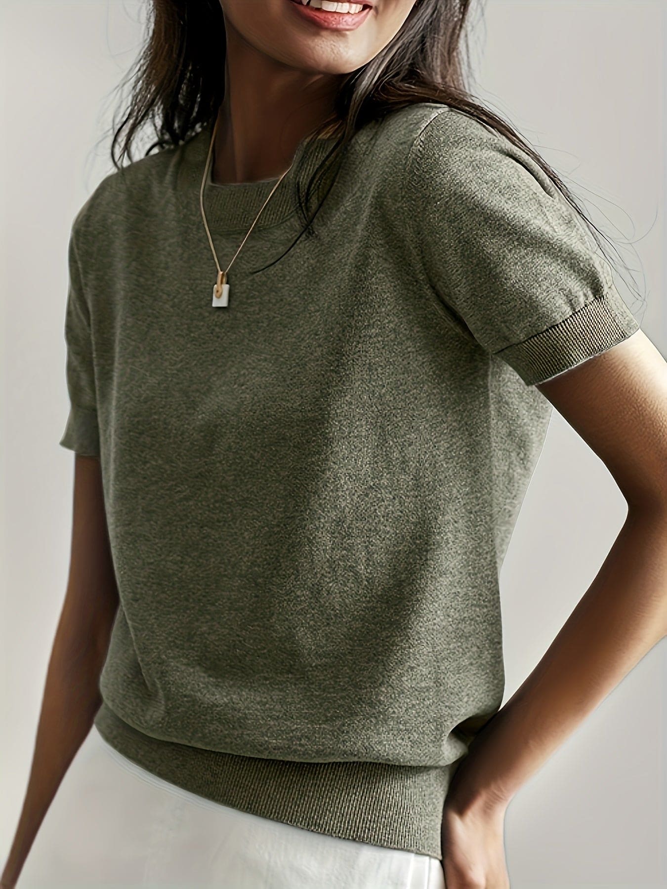 Kvinde iført en fintstrikket kortærmet sweater med rund hals og afslappet pasform, stylet med en lys nederdel og en guldfarvet halskæde._9