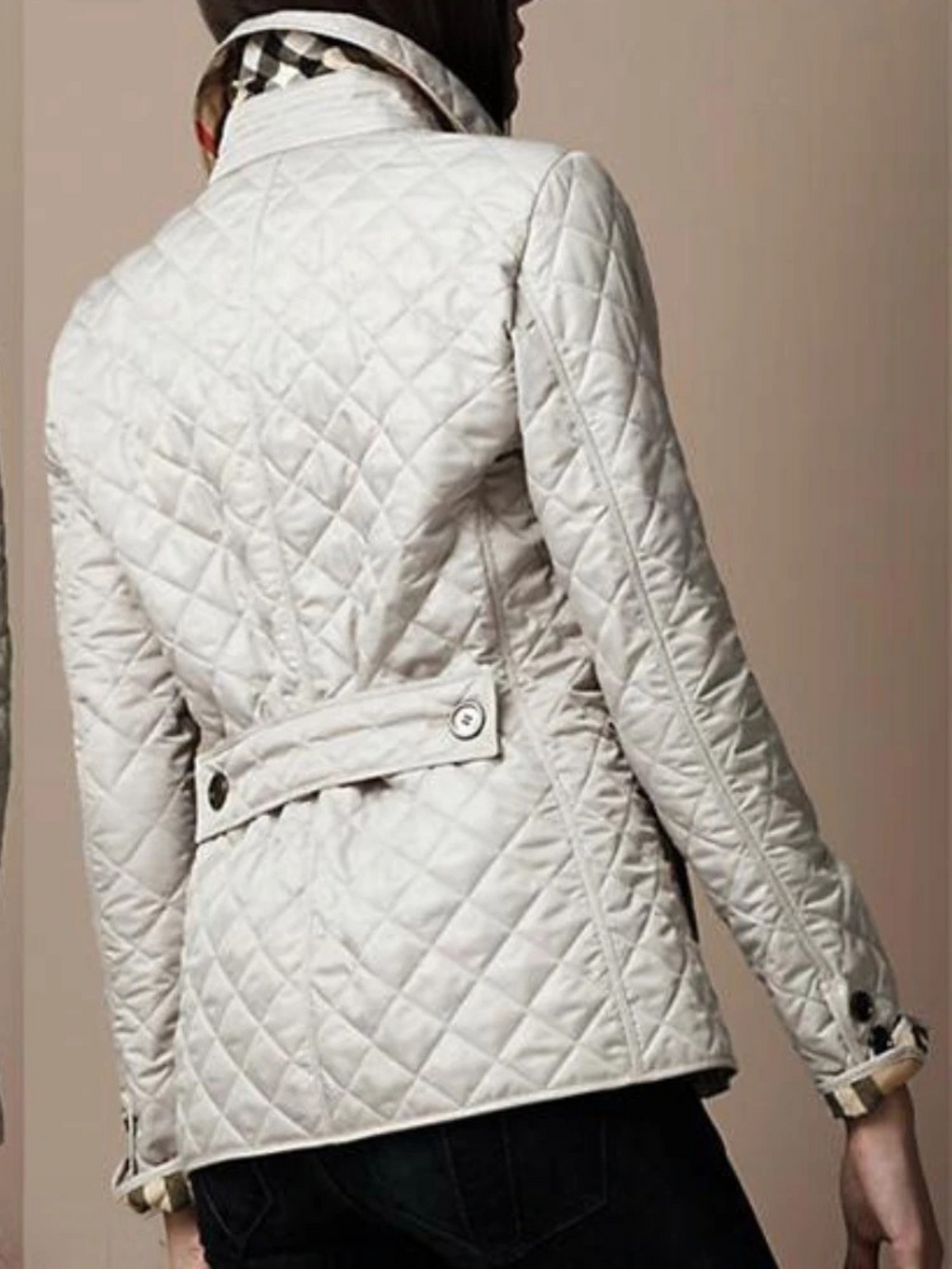 Kvinde i quiltet jakke med opretstående krave, trykknapper foran og sidelommer, båret over t-shirt og jeans._3