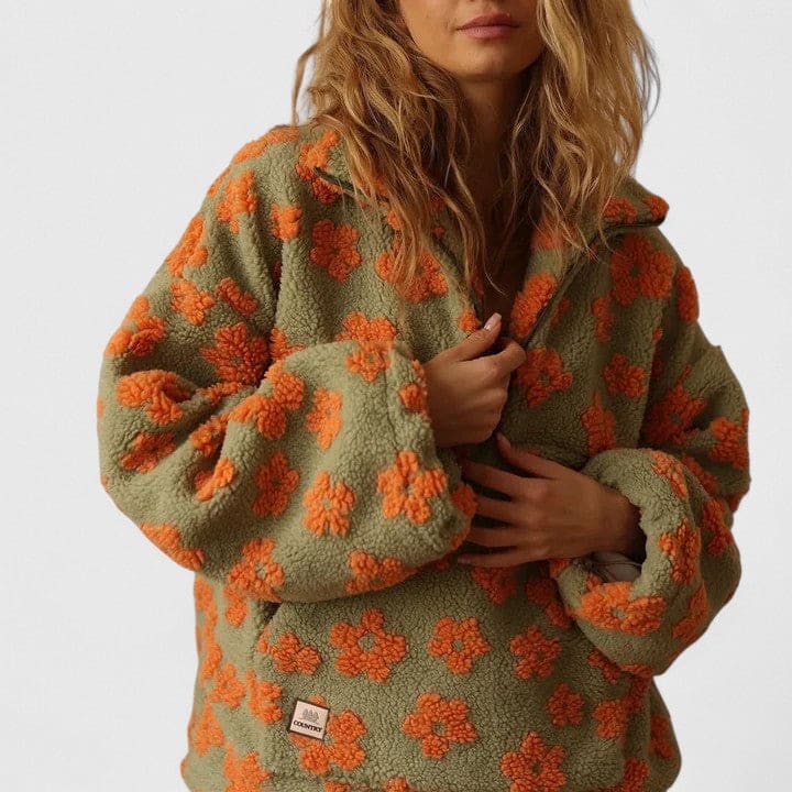 Kvinde iført en fleece sweater med blomstermønster og halv lynlås foran, fotograferet mod lys baggrund._7